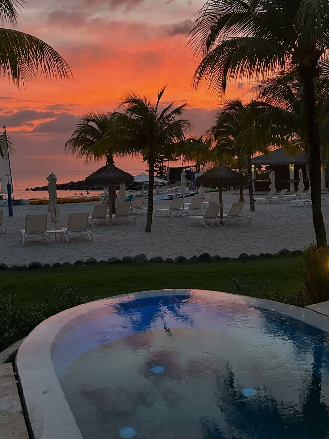 A private plunge pool looking out over palm trees and a beach at an orange sunset